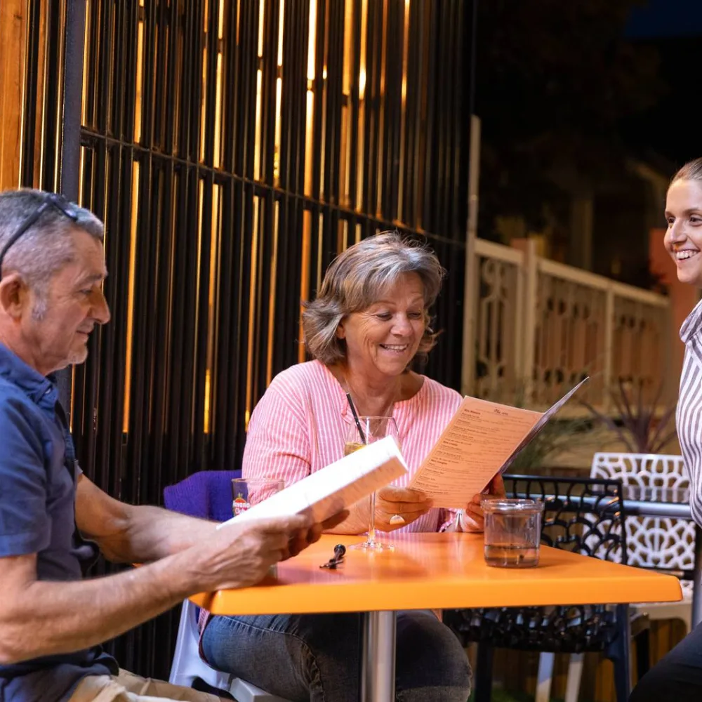 Une serveuse souriante auprès de deux clients en terrasse